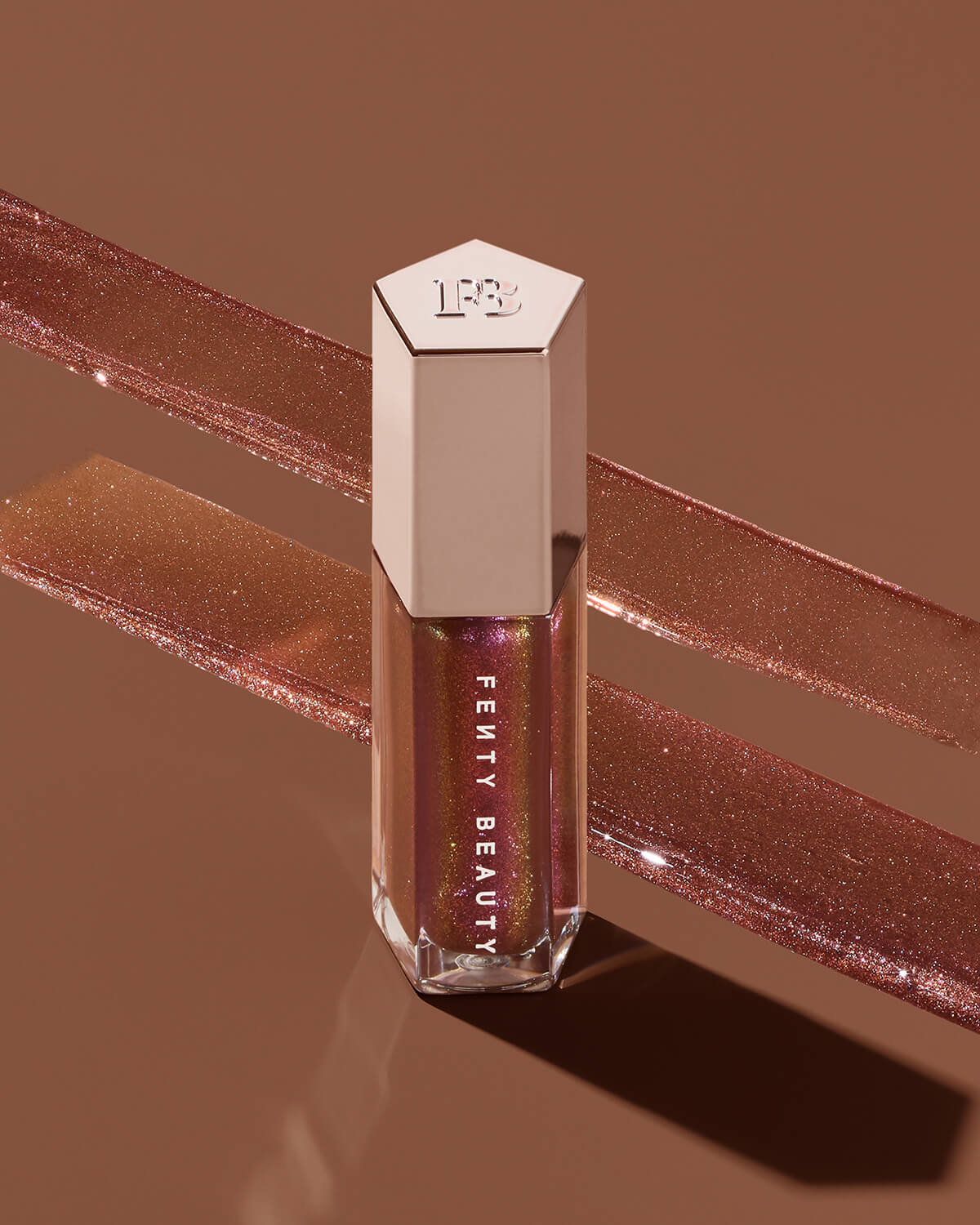 A closed tube of Gloss Bomb Universal Lip Luminizer with the lip gloss texture in the background.