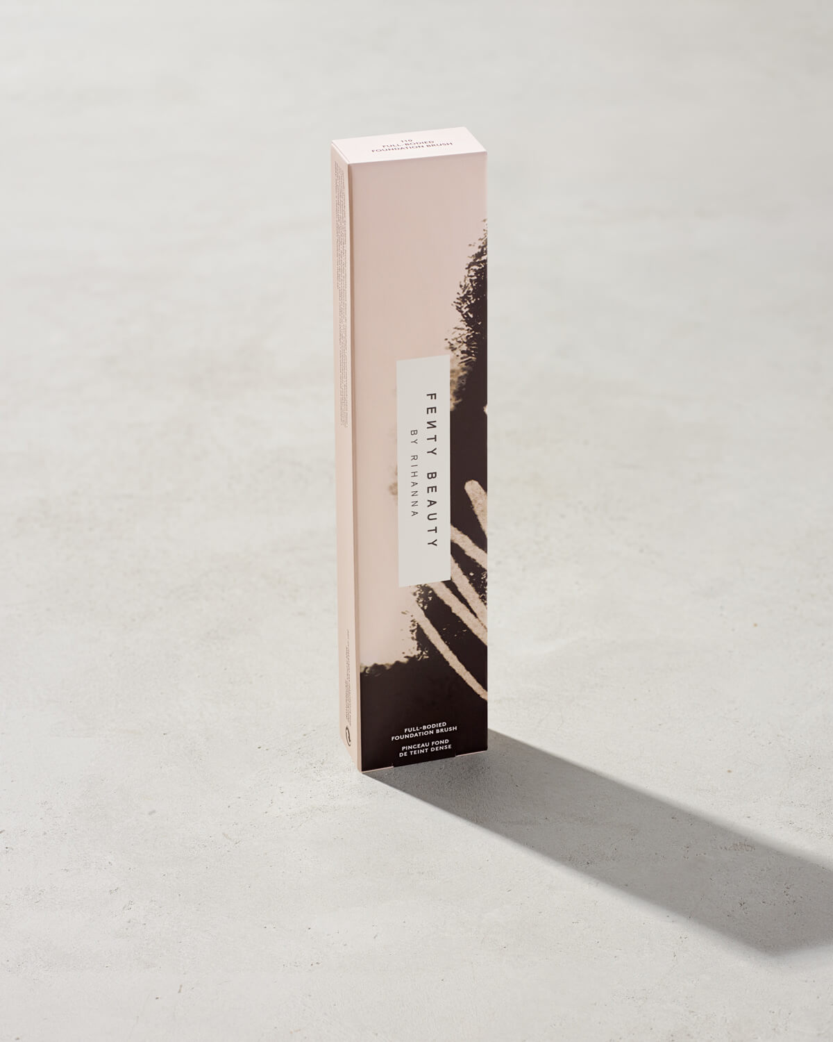 Packaging of the Full-Bodied Foundation Brush 110, featuring pink and black designs, standing upright on a concrete backdrop.