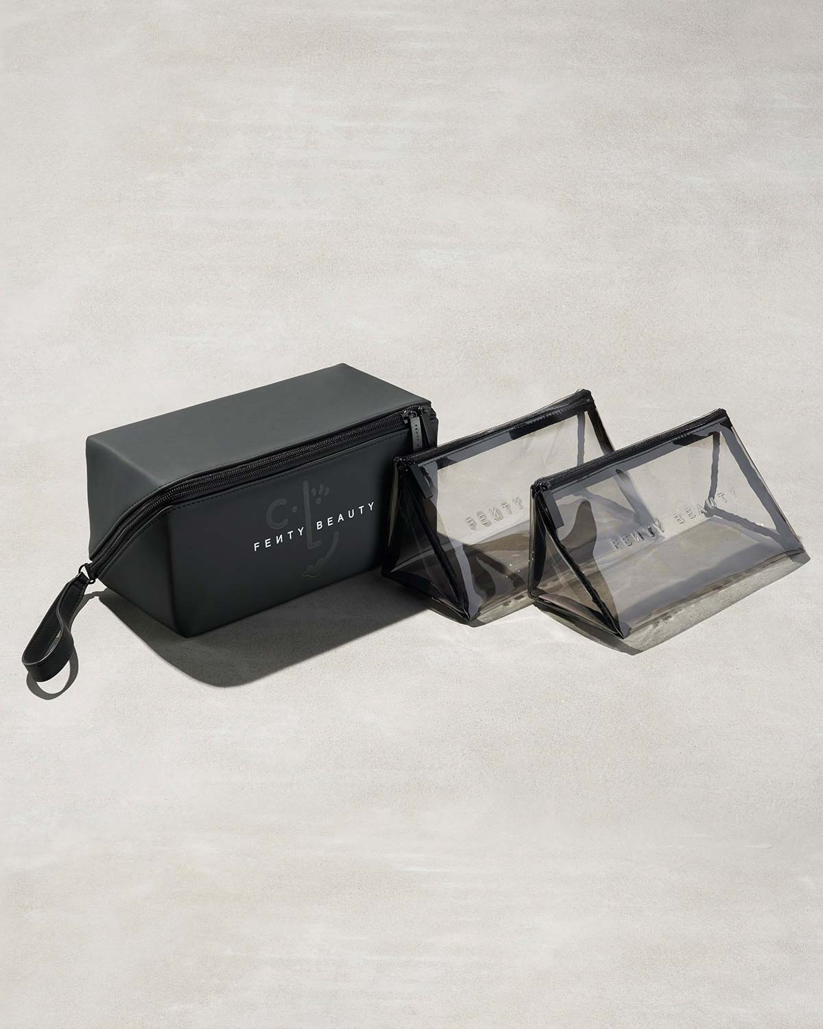 One black rectangular and two triangular clear bags with Fenty branding on a gray background