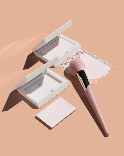 Open containers of Invisimatte Setting Powder, its refill and a setting brush on a peach background.