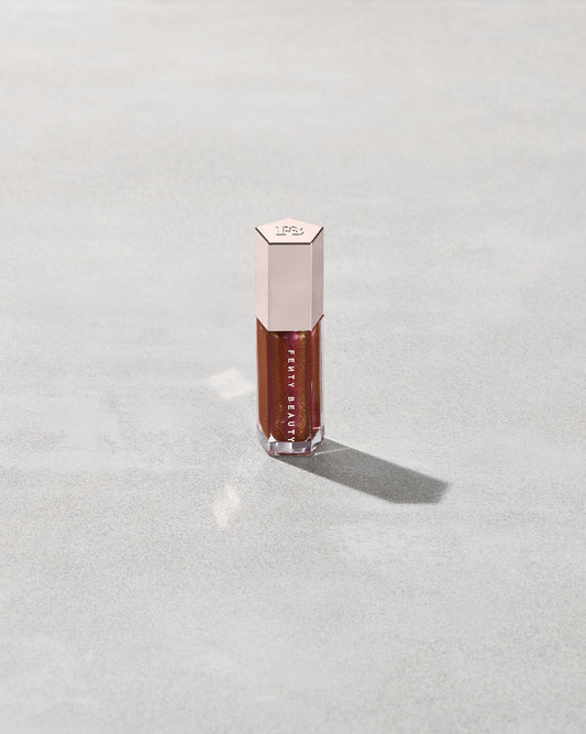 A close tube of Gloss Bomb Universal Lip Luminizer in the shade Hot Chocolit Fantasy on a grey background.
