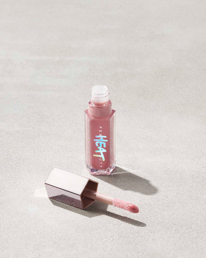 open tube of Fenty Beauty Gloss Bomb Heat Universal Lip Luminizer + Plumper in shade Fussy Heat with doe foot applicator on concrete background