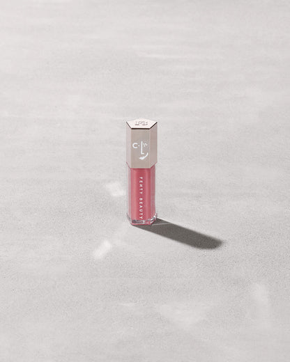 A closed tube of Gloss Bomb Universal Lip Luminizer in the shade Candy Soda on a grey background.