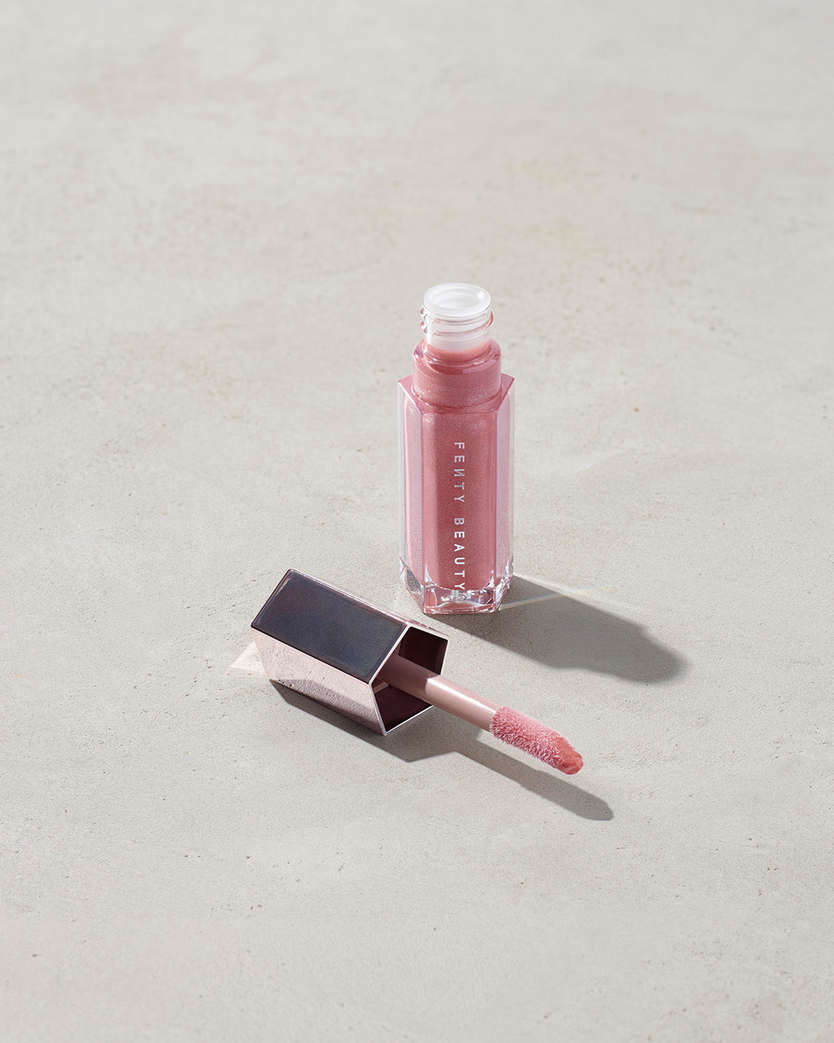 An open tube of Gloss Bomb Universal Lip Luminizer in the shade Fu$$y on a grey background.