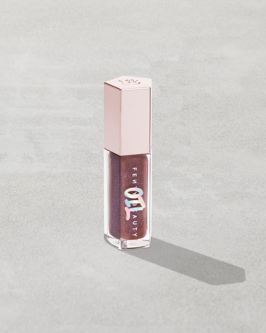 Gloss Bomb Oil Luminizing Oil and Gloss in shade Rose Amber product against a concrete background.