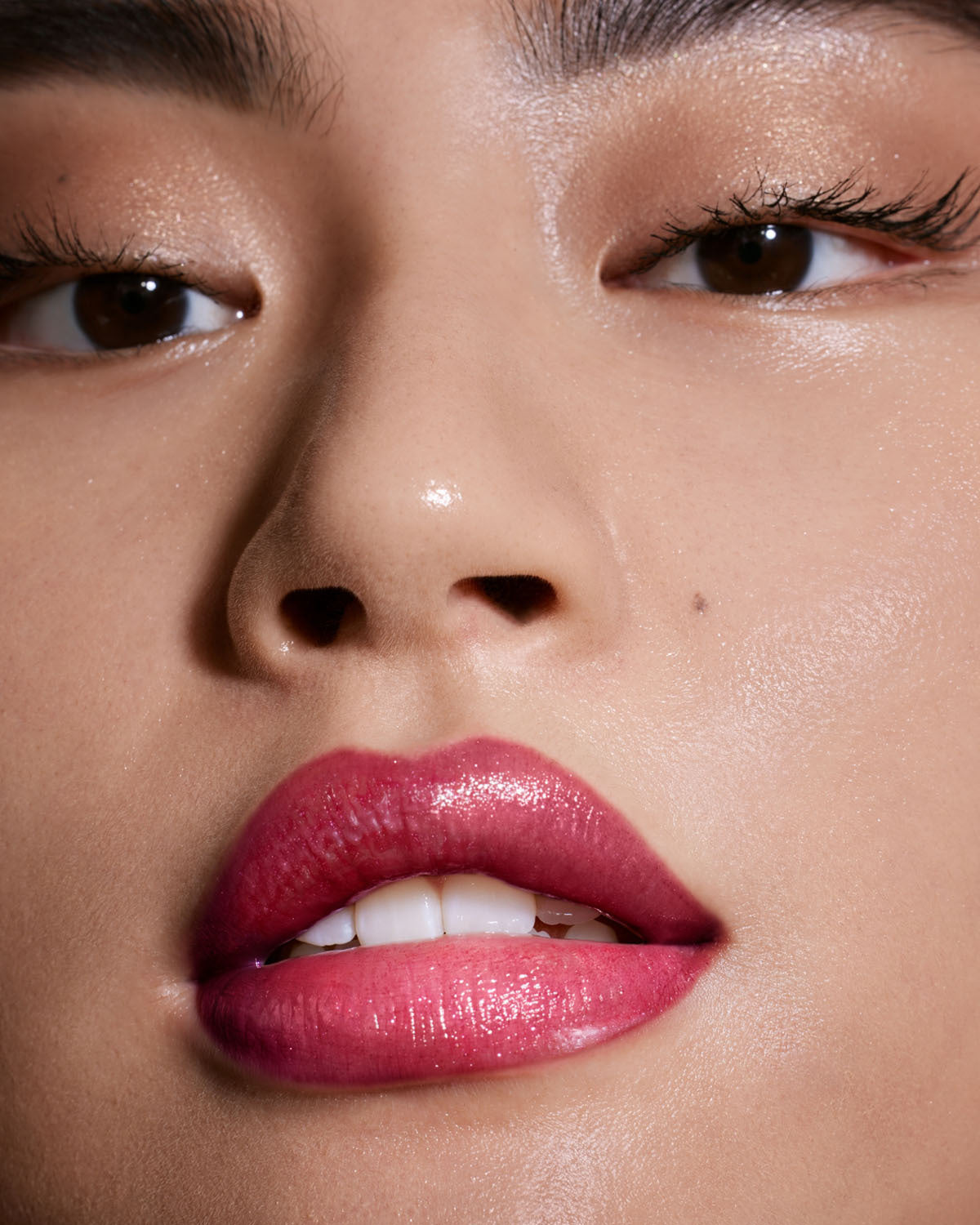 Close-up of a light-toned model's face wearing Gloss Bomb Universal Lip Luminizer in the shade Fuchsia Flex.