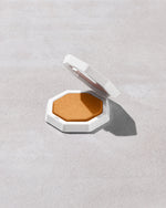 Open product shot of Demi'glow Light-Diffusing Highlighter in shade Rich Hunnie on a concrete backdrop.