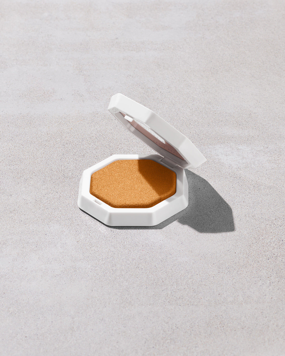 Open product shot of Demi'glow Light-Diffusing Highlighter in shade Rich Hunnie on a concrete backdrop.