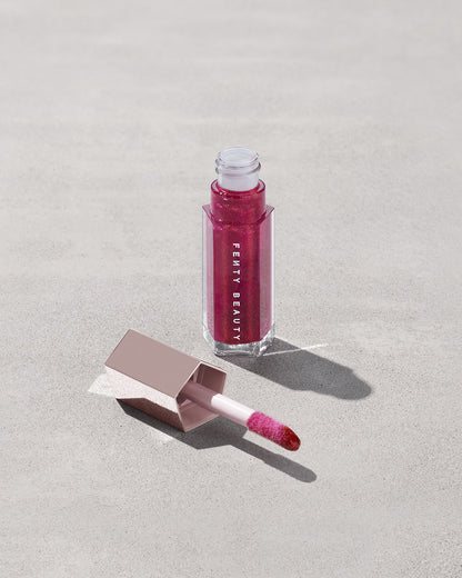 An open tube of Gloss Bomb Universal Lip Luminizer in the shade Fuchsia Flex on a grey background.